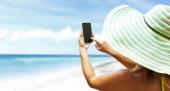 PO-24544-123RF-kurhan_123RF-Urlauberin_mit_Hut_macht_ein_Foto_am_Strand_mit_einem_Smartphone_s